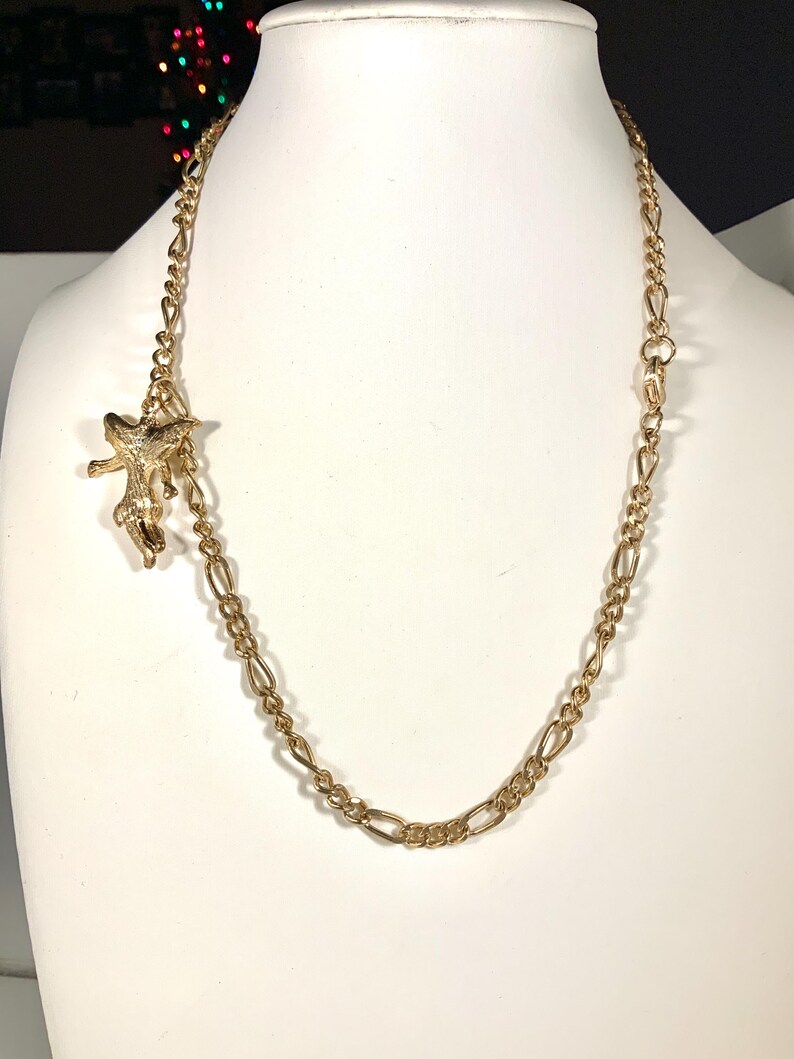 May include: A gold-colored necklace with a starfish pendant. The necklace features a chain with alternating oval and elongated links. The starfish pendant is detailed and hangs from a smaller chain.