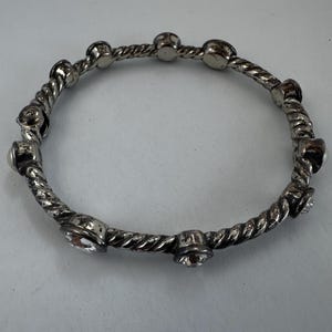 May include: Silver bangle bracelet with a twisted rope design. The bracelet has small, round, clear crystal accents. The bracelet is circular and appears to be made of metal.