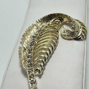 Beautiful, goldtone fancy feather brooch with clear round rhinestones. Matching clip on earrings.