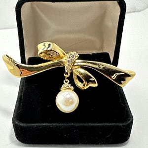 Vintage, goldtone brooch with dangling faux pearl and clear rhinestones. Unmarked