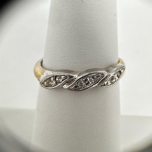 May include: A silver and gold band ring with a row of small clear stones set in the center.