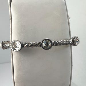 May include: Silver bracelet with a twisted rope design. The bracelet features three clear crystals, round and oval-shaped. The bracelet is displayed on a white surface.