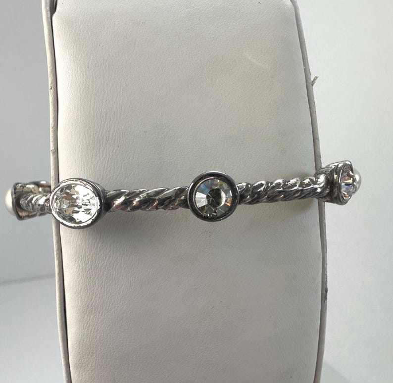 May include: Silver bracelet with a twisted rope design. The bracelet features three clear crystals, round and oval-shaped. The bracelet is displayed on a white surface.