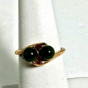 May include: A gold ring with two dark green round stones set in a wave-like design.
