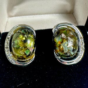 May include: A pair of silver tone clip-on earrings with green and gold iridescent glass stones.