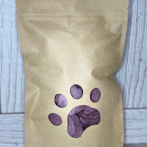 May include: A brown paper bag with a paw print cut-out. The cut-out reveals purple dog treats inside the bag.