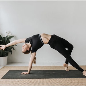 Puede incluir: Una persona con ropa deportiva negra realiza una postura de yoga en una esterilla de yoga negra. La persona está en una postura de puente con los brazos extendidos y la cabeza inclinada hacia atrás.