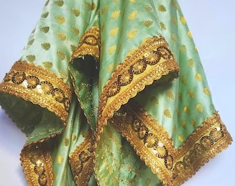 May include: A draped, light green fabric with gold-colored leaf patterns and ornate gold trim. The trim features intricate sequin and bead detailing. Gold tassels hang from the bottom edges, adding to the decorative appeal.