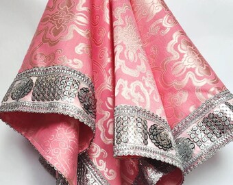 May include: Pink fabric with a gold floral pattern and silver sequin trim. The fabric is draped, revealing the intricate design and decorative tassels. The trim features silver sequins and floral accents, adding a touch of elegance.