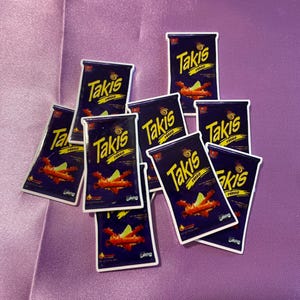 May include: A collection of nine Takis Fuego snack bags. The bags are purple with a white border and feature a red and orange image of Takis chips. The text "Takis Fuego" is printed in white on the bags.