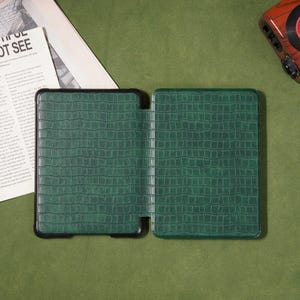 May include: Green faux-leather tablet case with a crocodile skin texture. The case is open, revealing the interior. The case has a black border and is set against a green background.