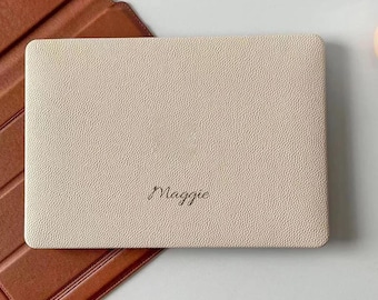 May include: A rectangular, cream-colored tablet case with a textured, pebbled surface featuring the name Maggie embossed in a dark, cursive script. The case is positioned partially over a brown, smooth-textured, folding protective cover.