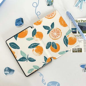 May include: A white e-reader cover with a pattern of orange citrus fruit and green leaves. The cover is folded open to show the front and back sides. The front side has the words "Front" written in blue. The back side has the words "Back" written in blue.