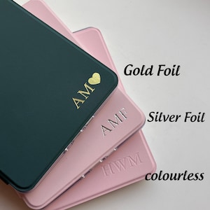 May include: Three rectangular cases in dark green and light pink with personalized monograms. The top case features gold foil initials AM with a heart, the middle case has silver foil initials AMF, and the bottom case has colorless embossed initials HWM.