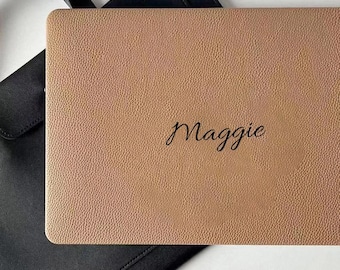 May include: A rectangular tan laptop skin with a textured surface featuring the name Maggie in black cursive script, positioned over a black laptop sleeve. The skin covers the top surface of the device, displaying a clear, legible personalization.