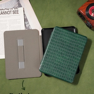May include: A gray tablet case with a built-in strap is open, revealing a black tablet. A green, textured tablet case is on top. The text "Built in strap" is below the gray case.