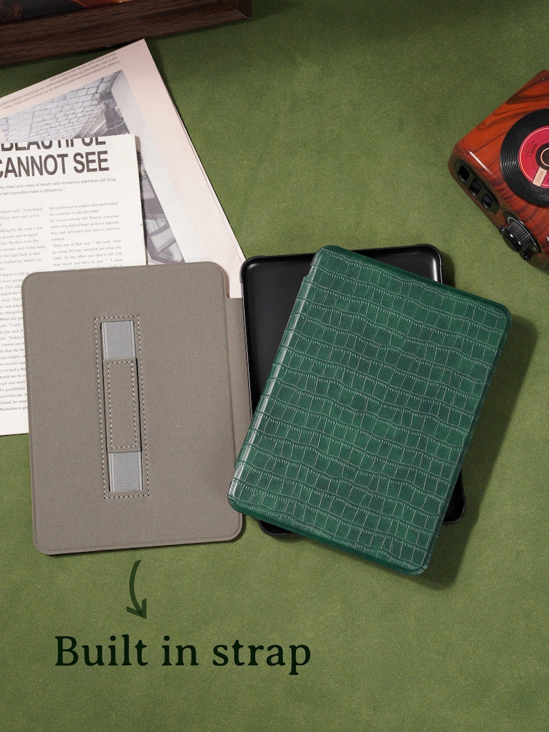 May include: A gray tablet case with a built-in strap is open, revealing a black tablet. A green, textured tablet case is on top. The text "Built in strap" is below the gray case.