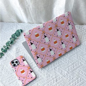 Può includere: Una custodia per laptop e una custodia per smartphone abbinata, entrambe con uno sfondo rosa chiaro con un motivo ripetuto di fantasmi bianchi con cappelli da strega neri, zucche arancioni, piccole stelle nere e sottili linee a nastro arancioni.