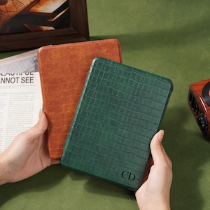 May include: Two leather-textured tablet cases, one in a rich brown and the other in a deep green. The green case features the initials "CD" in the lower right corner. The cases are rectangular and appear to be new.