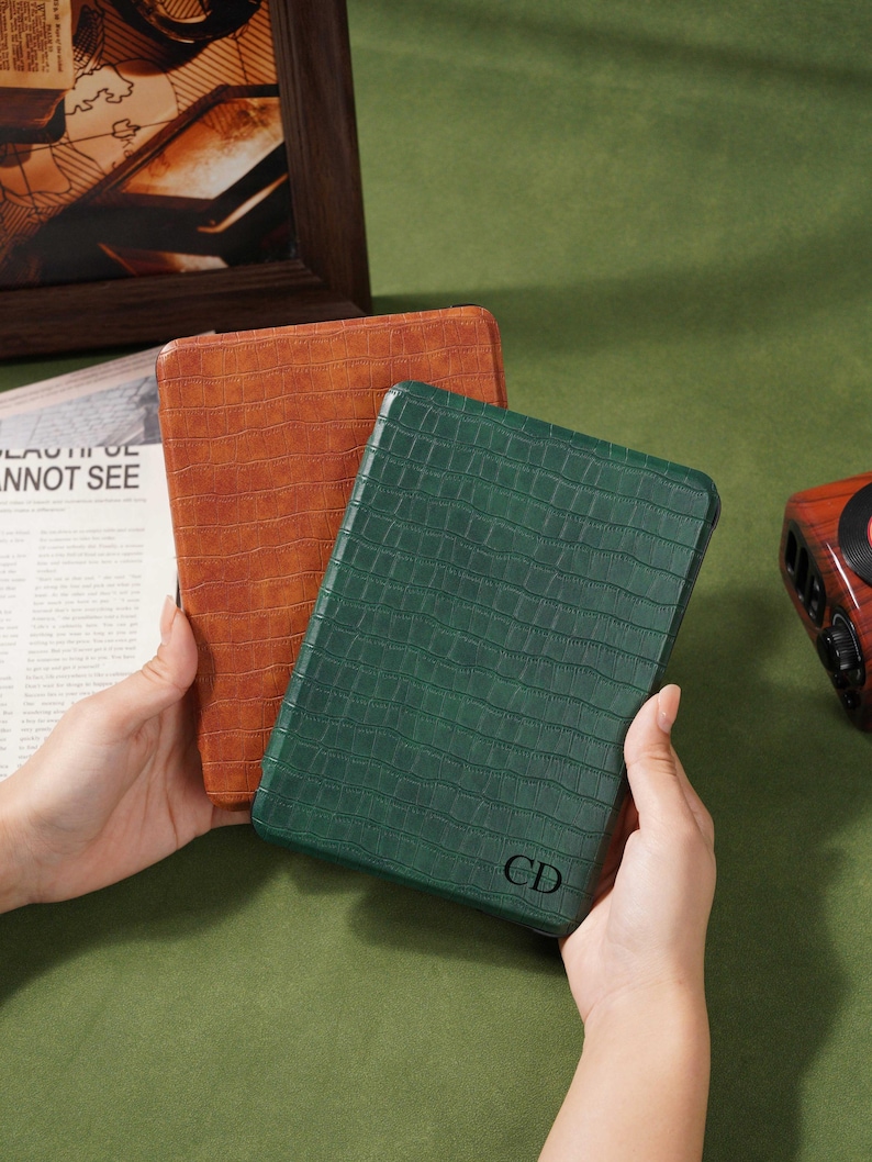 May include: Two leather-textured tablet cases, one in a rich brown and the other in a deep green. The green case features the initials "CD" in the lower right corner. The cases are rectangular and appear to be new.