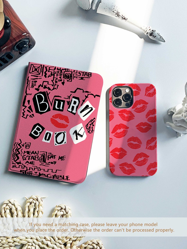 May include: Pink phone case with a red lip print and a pink notebook-style case with the words "BURN BOOK" in a graffiti style. The notebook case has additional text and doodles in black.