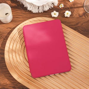 May include: A rectangular e-reader device featuring a solid, vibrant hot pink protective cover. The device has a smooth, matte-textured surface and rounded corners, presenting a clean, minimalist aesthetic without any visible buttons or markings.