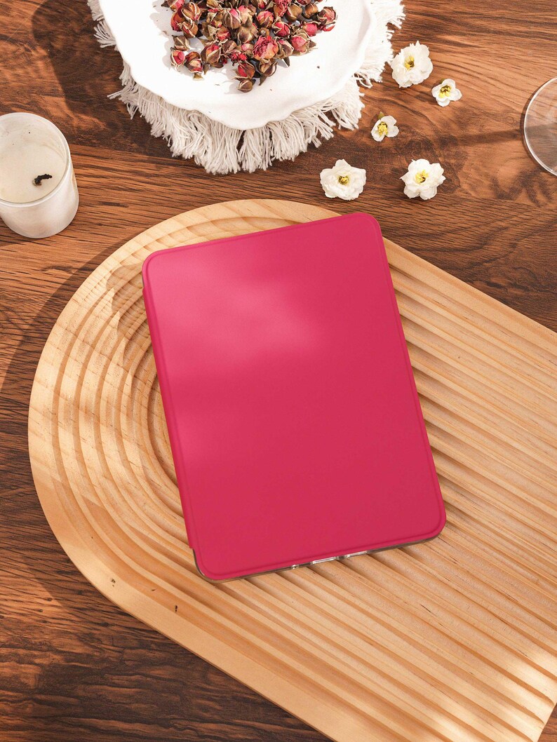 May include: A rectangular e-reader device featuring a solid, vibrant hot pink protective cover. The device has a smooth, matte-textured surface and rounded corners, presenting a clean, minimalist aesthetic without any visible buttons or markings.