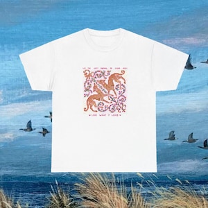 以下が含まれることがあります： 白いTシャツ。カラフルなデザインで、「LET THE SOFT ANIMAL OF YOUR BODY」と「LOVE WHAT IT LOVES」の文字が入っています。茶色の動物の姿と花柄が特徴です。