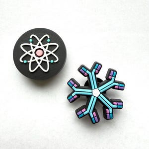 May include: Two decorative accessories. One is a black circle with a white atom design, a pink center, and teal accents. The other is a snowflake design with blue, pink, and purple accents.