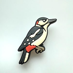 May include: A decorative woodpecker figurine. The bird has a black and white body with red detailing on its head and wings. It is perched on a branch, with a gray and beige colour scheme.