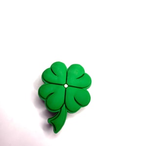 Pode incluir: Um amuleto de trevo de quatro folhas verde brilhante, com um ponto central branco e um caule curvo. O trevo está sobre um fundo branco. Símbolo de boa sorte.