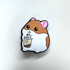 May include: A brown and white cartoon hamster with pink ears is holding a brown cup with a straw and boba pearls. The hamster is smiling.