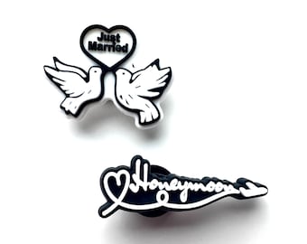 May include: Two black and white shoe charms. One charm features two doves with a heart that says "Just Married". The other charm says "Honeymoon" in a cursive font.
