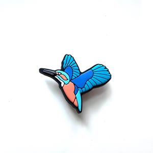 May include: A colorful bird-shaped charm in flight, featuring shades of blue, coral, and black. The charm has a detailed wing design and is set against a white background. This decorative charm is suitable for various craft projects.
