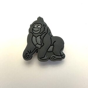 May include: A black rubber charm depicting a cartoon gorilla with a happy expression.