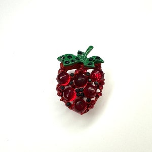 May include: A red rhinestone strawberry brooch with a green leaf. The strawberry is made of metal and has a shiny finish.