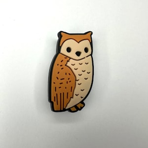 May include: A brown and white owl with black eyes and a black outline. The owl is standing on a white background.
