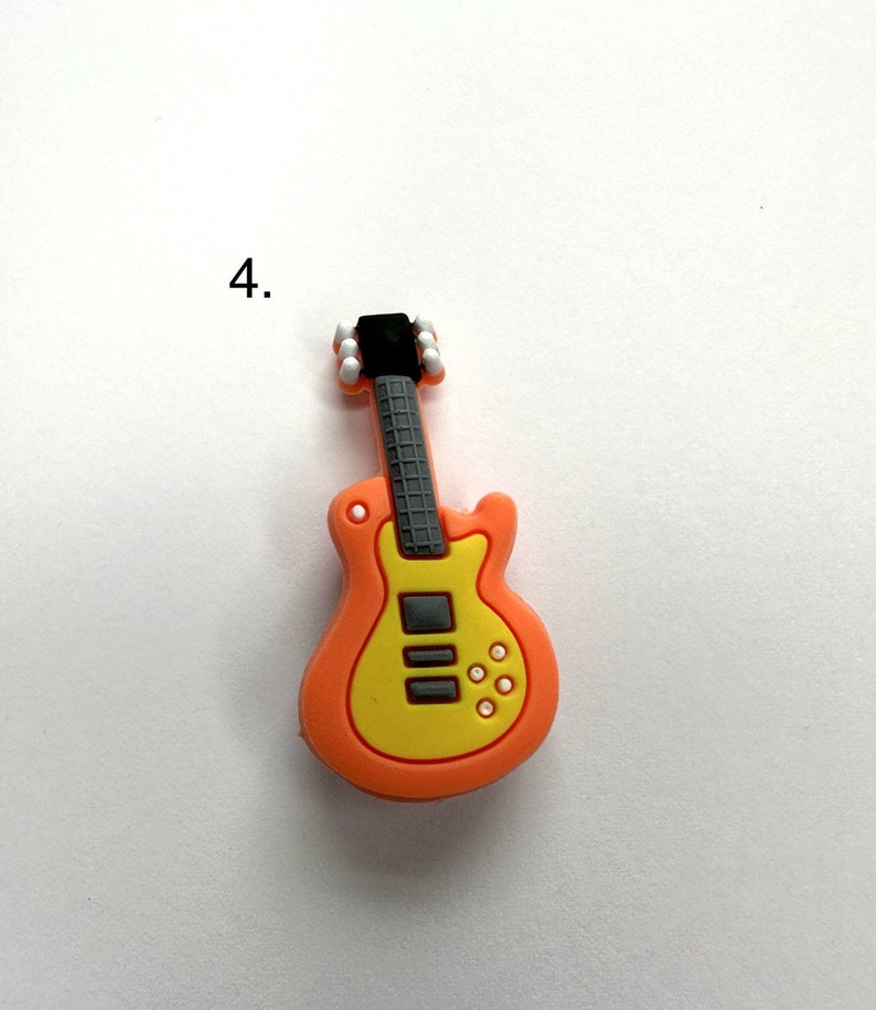 May include: A small orange and yellow plastic guitar charm with black details. The guitar has a black pickguard and white knobs.