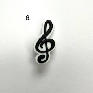 May include: A black treble clef charm with a white outline. The charm is on a white background.