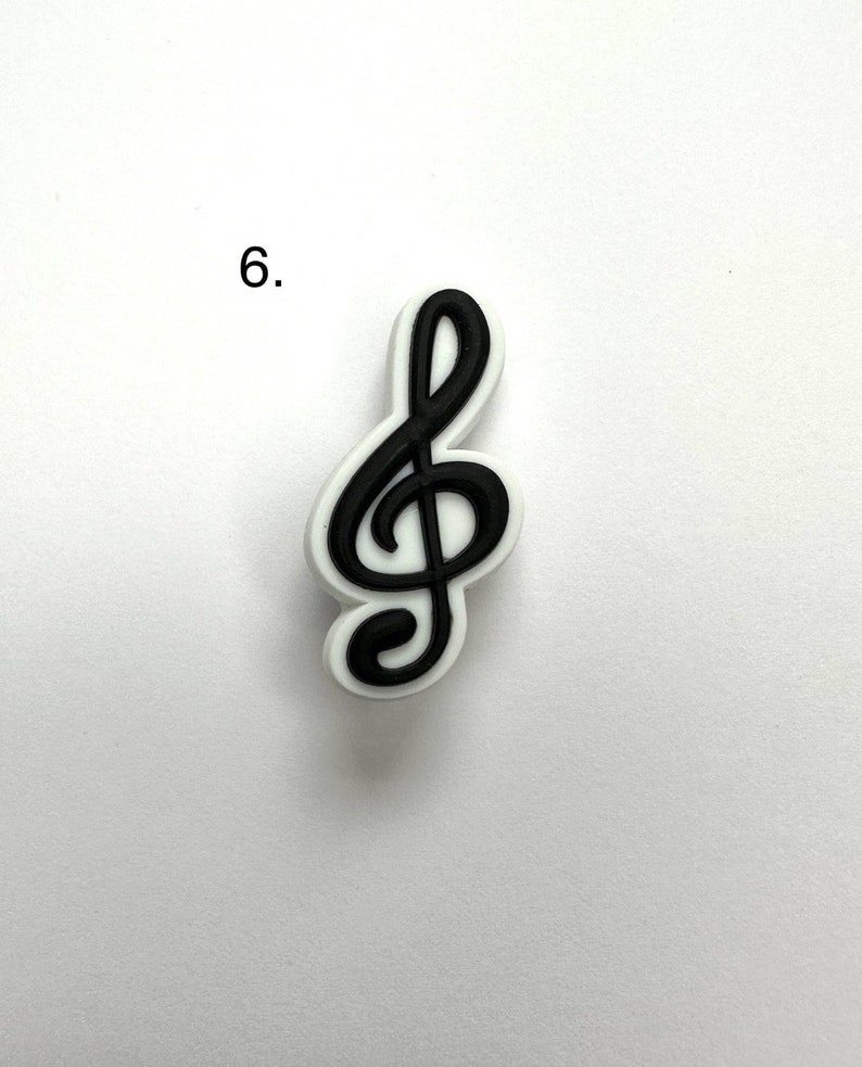 May include: A black treble clef charm with a white outline. The charm is on a white background.