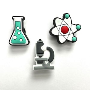 May include: Three science-themed charms: a flask with teal liquid and bubbles, a microscope, and an atom model. The charms are black, white, gray, teal, and red. These charms are ideal for science enthusiasts.