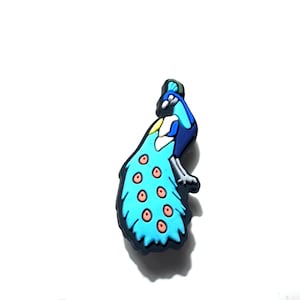 May include: A colorful peacock-shaped charm. The charm features a blue, turquoise, and black design with a fan of feathers. The feathers have small, round, orange accents. The charm is likely made of rubber or plastic.
