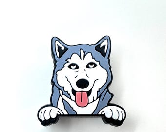 May include: A blue and white husky dog with a pink tongue sticking out peeks over a black surface. The dog is cartoon-style and has a friendly expression.