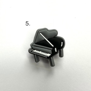 May include: A gray and black grand piano charm. The piano has white keys and a gray lid.