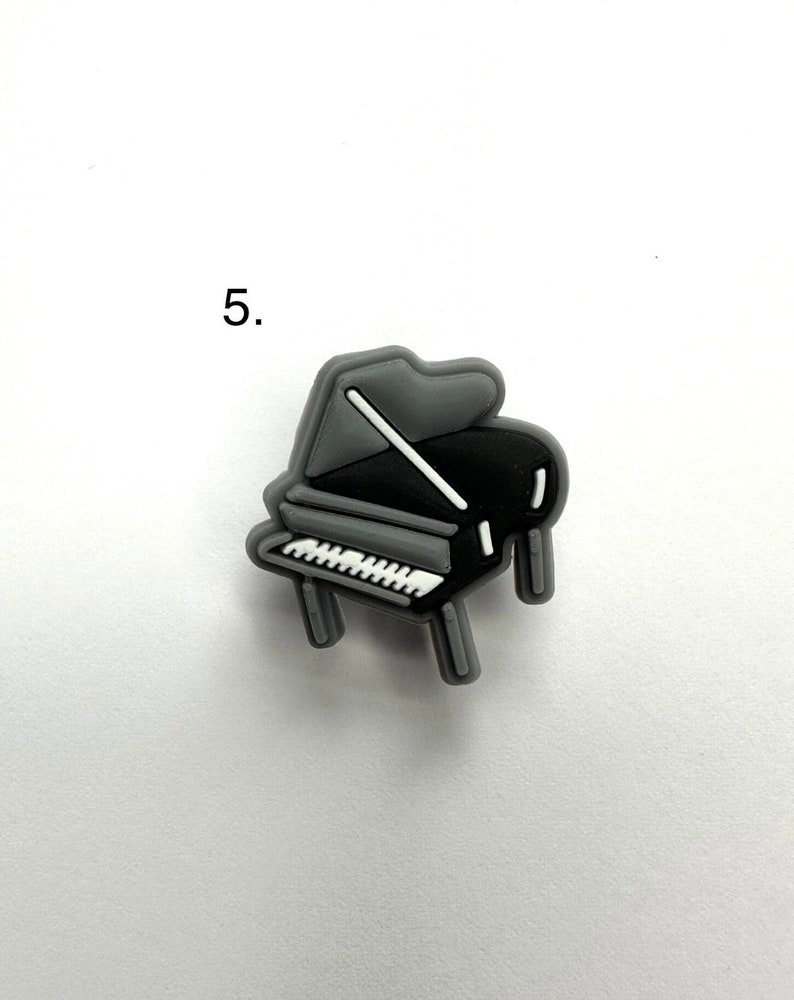 May include: A gray and black grand piano charm. The piano has white keys and a gray lid.