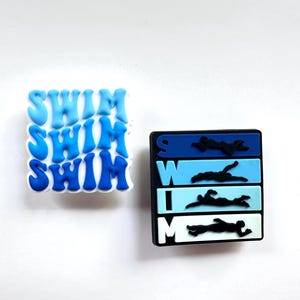 May include: Two blue and white charms with the word "SWIM" repeated three times on one charm and a swimmer silhouette with the word "SWIM" on the other charm.