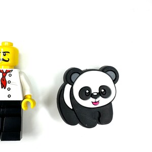 Puede incluir: Un amuleto de panda blanco y negro con una sonrisa rosa. El amuleto est&aacute; hecho de goma y tiene un dise&ntilde;o 3D.