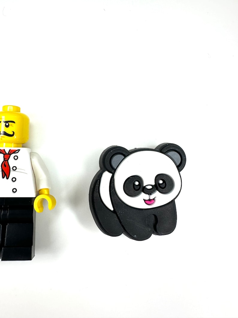 Puede incluir: Un amuleto de panda blanco y negro con una sonrisa rosa. El amuleto est&aacute; hecho de goma y tiene un dise&ntilde;o 3D.