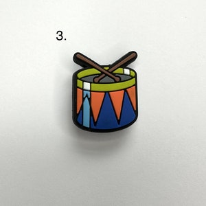May include: A small, colorful toy drum with two drumsticks crossed over the top. The drum is blue with orange and white stripes and a green rim. The drumsticks are brown.