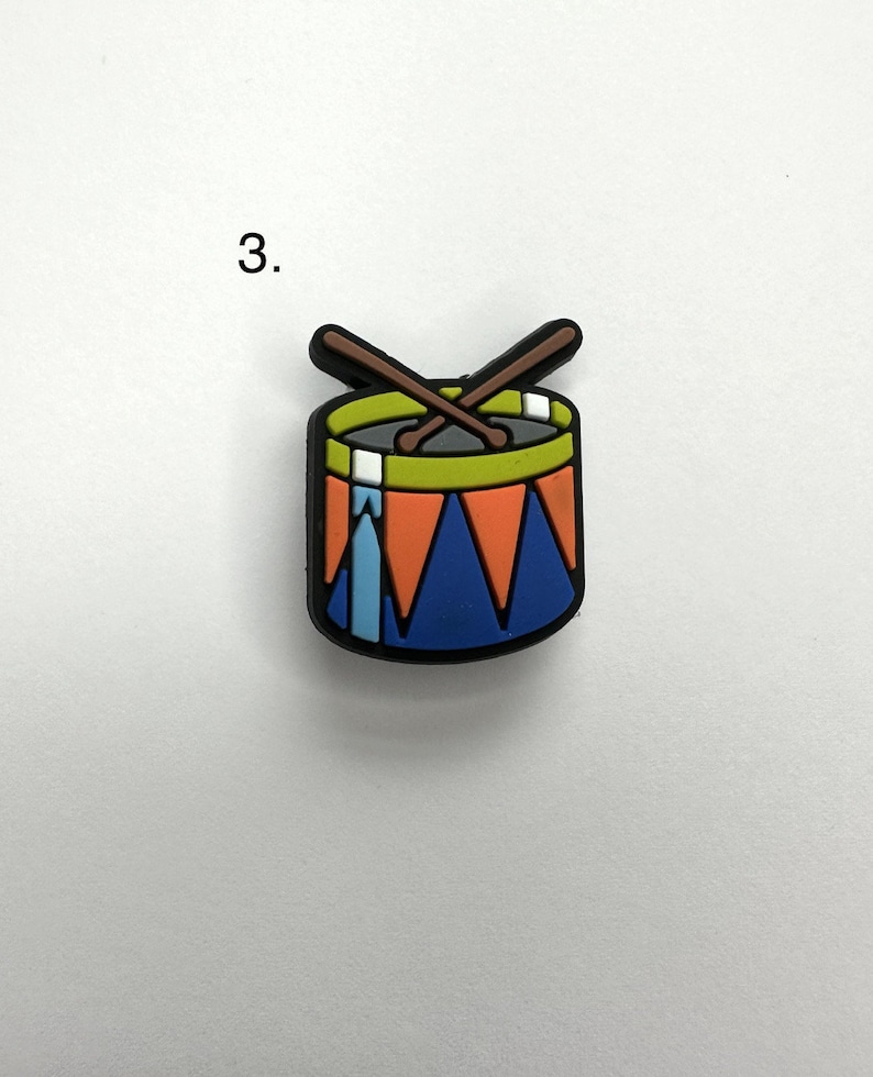 May include: A small, colorful toy drum with two drumsticks crossed over the top. The drum is blue with orange and white stripes and a green rim. The drumsticks are brown.